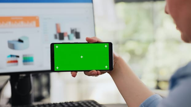 Analyst examines greenscreen software while she holds smartphone, isolated copyspace template shown on screen. Specialist checking blank mockup layout on mobile device. Handheld shot. Close up.
