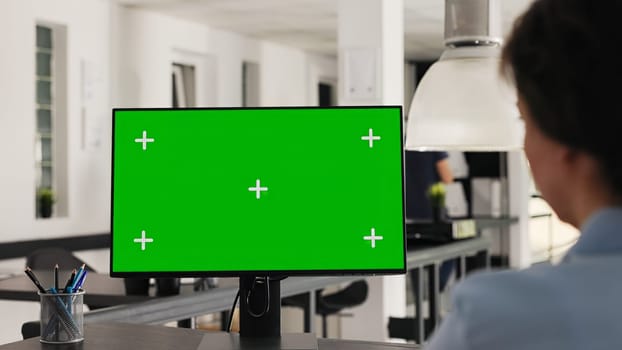 Office manager uses greenscreen on pc and working with isolated monitor display for business development. Woman looking at computer showing blank chromakey layout on desk. Handheld shot.