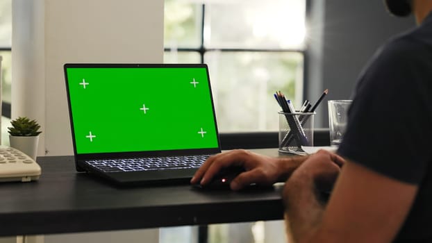 Male employee looks at greenscreen on laptop display, checking isolated chromakey layout in office coworking space. Businessman examining blank copyspace template at modern desk.