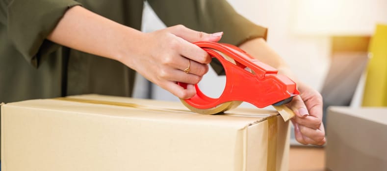 Asian young woman hand packing shipment box with transparency tape at home office, happy freelance and packing cardboard box delivery products to customers, Startup small business, Moving day