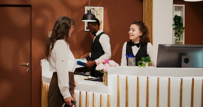 Retired woman arriving at hotel resort, asking receptionist about senior travel offers for wellness and recreation. Employee greeting guest at reception, ensuring easy check in and pleasant stay.
