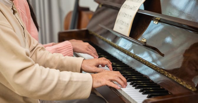 Family. Young woman teaching piano for senior man teaching, happy daughter and elderly father with eyeglasses relaxation playing piano together in living room at home, lifestyle life after retirement