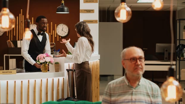 Retired adult at front desk does check in process in luxury hotel lobby. Reception staff assisting traveller with registration to ensure pleasant stay, all inclusive room accommodation.