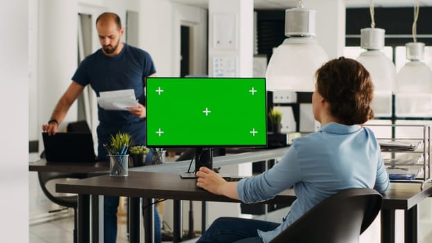 Specialist looking at greenscreen template on desktop monitor in small business agency workplace. Person checking isolated display showing blank chromakey mockup, problem solving. Tripod shot.