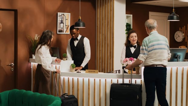Retired couple arrive at hotel reception, talking to front desk staff before working on check in process. Tourists with luggage travelling on holiday to have fun, hotel concierge luxury services.