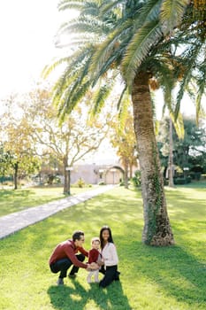 Mom and dad squatted near a little girl on a green grass. High quality photo