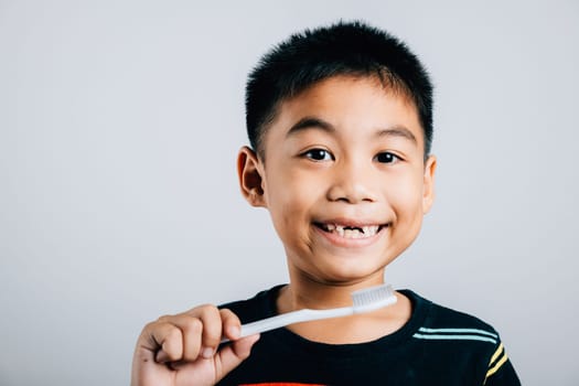 An Asian child with a missing upper milk tooth holds a toothbrush promoting dental hygiene and learning. Isolated on white background showcasing dental care routine. Children dentist routine