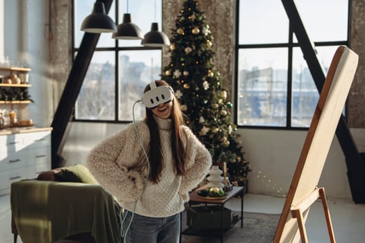 Surrounded by a Christmas tree, a beautiful young woman uses a virtual reality headset. High quality photo