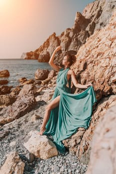 Woman green dress sea. Woman in a long mint dress posing on a beach with rocks on sunny day. Girl on the nature on blue sky background