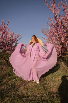 Woman blooming peach orchard. Against the backdrop of a picturesque peach orchard, a woman in a long pink dress and hat enjoys a peaceful walk in the park, surrounded by the beauty of nature