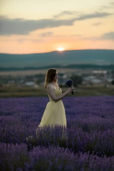 Woman poses in lavender field at sunset. Happy woman in yellow dress holds lavender bouquet. Aromatherapy concept, lavender oil, photo session in lavender.