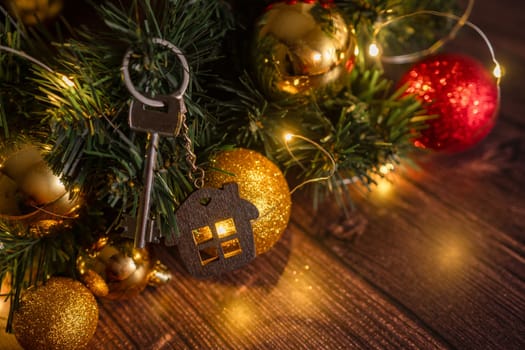 Gift key house with a keychain backdrop of Christmas tree. Building, design, project, moving to new house, mortgage, rent and purchase real estate. A gift for New Year, Christmas.