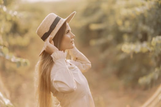 Woman with straw hat stands in front of vineyard. She is wearing a light dress and posing for a photo. Travel concept to different countries.