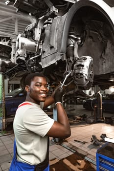 African male auto-mechanic repairing car brakes under the car in auto service close up