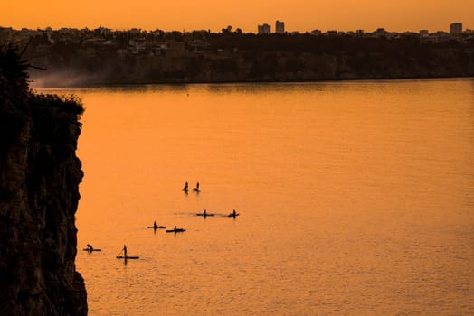 Adventurous people on a stand up paddle board is paddling during a bright and vibrant sunrise