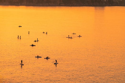 Adventurous people on a stand up paddle board is paddling during a bright and vibrant sunrise