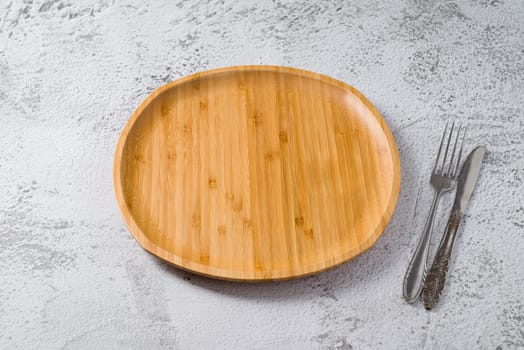 Wooden plate, fork and knife on white stone background. handmade kitchen utensils