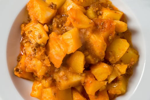 Minced meat and potato dish on white porcelain plate on stone table