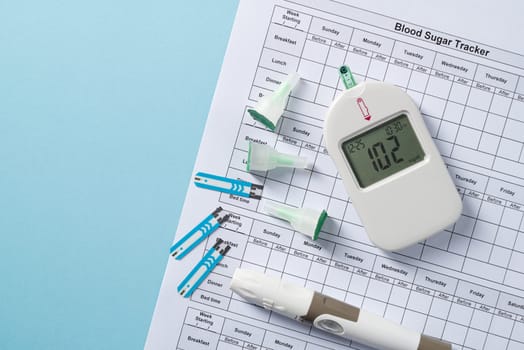 Top view of glucometer, lancet pen, strips and blood sugar tracker on blue background. diabetes test kit