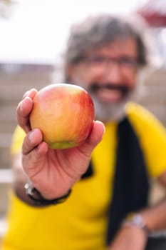 senior sports man showing an apple after workout, concept of healthy and active lifestyle in the middle age, selective focus on the apple