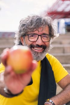 senior sports man showing an apple after workout, concept of healthy and active lifestyle in the middle age, focus on the smiling face