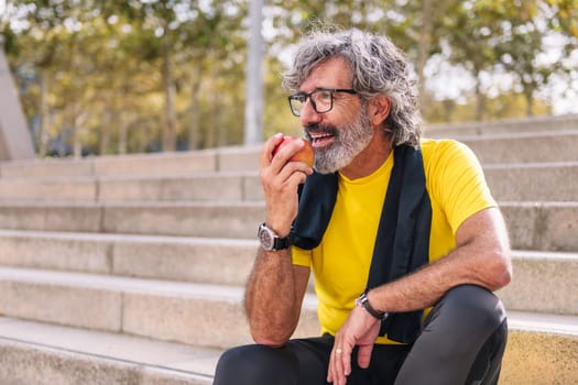 senior sports man rests eating an apple after a hard workout, concept of healthy and active lifestyle in the middle age, copy space for text