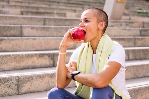 young sports woman with short hair rests eating an apple after a hard workout, concept of healthy and active lifestyle, copy space for text