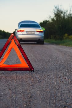 Broken silver luxury car emergency accident. Man driver installing red triangle stop sign on road. Sport automobile turned on blinkers technical problems on the road. Safety procedure when having vehicle broken down