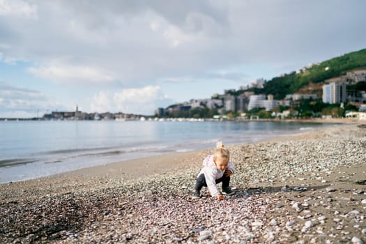 Little girl playing with pebbles on the beach squatting. High quality photo