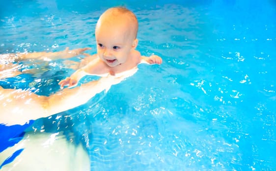 Adorable baby girl enjoying swimming in a pool with her mother early development class for infants teaching children to swim and dive. Swimming instructor doing exercises with a small child in the pool . High quality photo