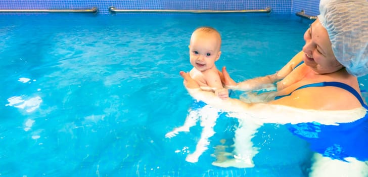 Adorable baby girl enjoying swimming in a pool with her mother early development class for infants teaching children to swim and dive. Swimming instructor doing exercises with a small child in the pool . High quality photo