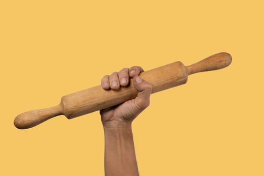 Hand holding a wooden rolling pin isolated on yellow background. High quality photo
