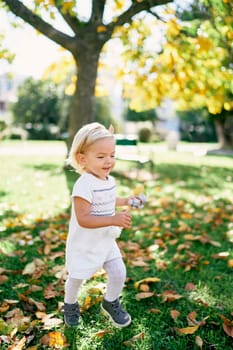Little girl with a soft toy in her hands walks along the lawn with fallen yellow leaves. High quality photo