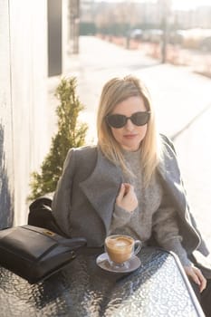 Young woman enjoying a coffee, sitting with mobile phone on the cafe terrace on the old city street during a sunny day. High quality photo