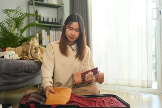 Pretty young woman checking clothes and stuff in luggage on floor in living room before travel trip.