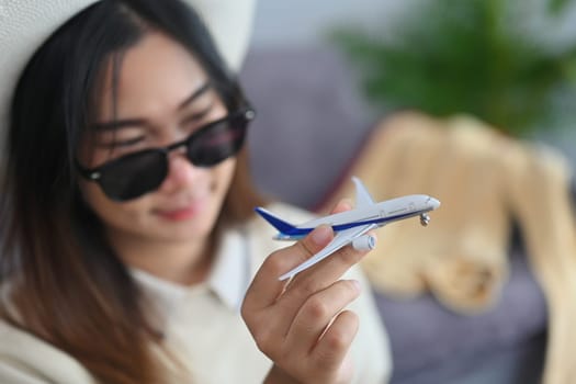 Happy young woman traveler in sunglasses holding airplane model. Traveling, vacation and transportation concept