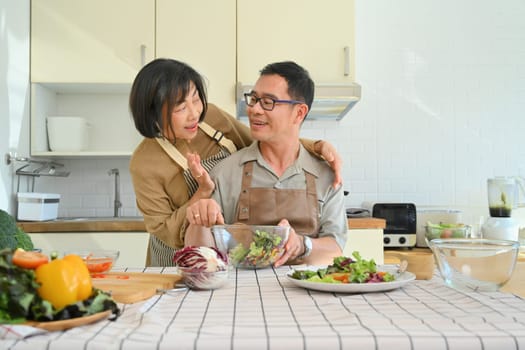 Beautiful senior couple preparing salad together at kitchen table. Healthy lifestyle concept