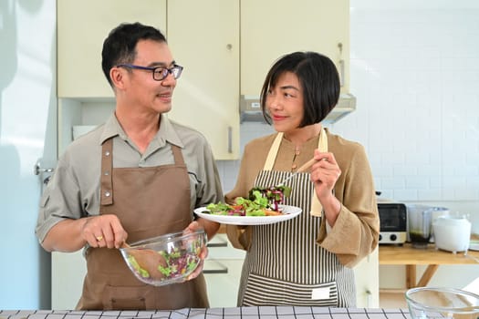 Happy middle age couple preparing vegetables salad together in the kitchen. Healthy lifestyle concept