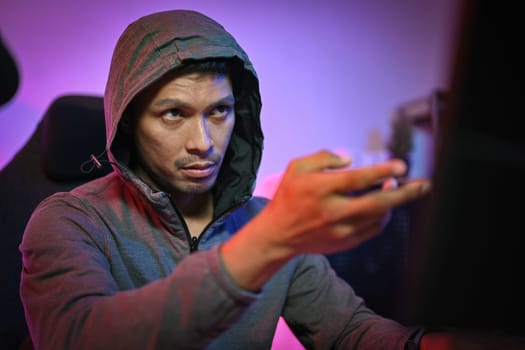 Young adult male in hoodie playing video games on computer with serious face expression.