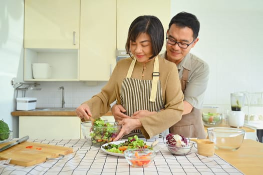 Loving middle age couple preparing healthy vegetables salad in kitchen. Happy senior lifestyle concept