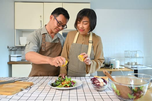 Middle age couple preparing healthy vegetables salad in kitchen. Happy senior lifestyle concept