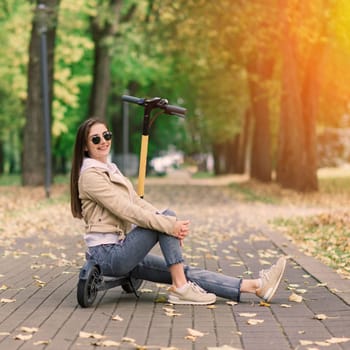 Young woman riding an electric scooter in autumn park. Green transport, traffic jam problems.