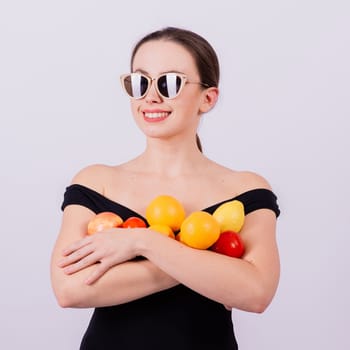 Smiling cool girl in a sun glasses in black swimsuit posing with fruits and laughing.