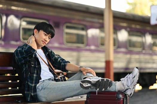 Asian male traveller sitting on bench waiting for train at railway station . Travel and lifestyle concept.