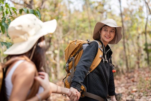 Cheerful romantic lesbian couple traveler with backpack on their backs go hiking through the forest in the mountains in summer.