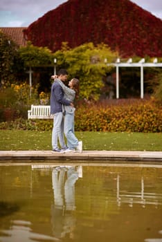 A couple in love hugs on the shore of a city pond in the European town. love story against the backdrop of autumn nature. romantic ambiance, couple goals, outdoor romance, seasonal charm, love in the city, autumnal vibes, European town, city pond, affectionate bonding, love story