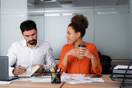 Two young businesspeople smiling while working with wireless technology in a modern workspace.