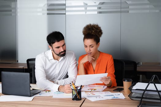 Two young businesspeople smiling while working with wireless technology in a modern workspace.