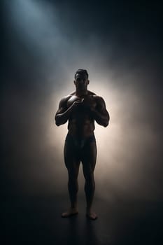 A man confidently stands in front of a spotlight, illuminating him on a dark stage.