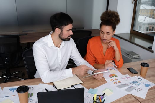 Two young businesspeople smiling while working with wireless technology in a modern workspace.